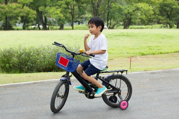 Il ragazzo asiatico guida una bicicletta al fondo della natura di verde del parco.