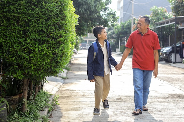 Il ragazzo asiatico in uniforme e zaino dopo la scuola sta camminando insieme al nonno in pensione Pare