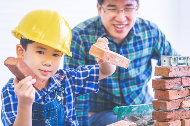 Il ragazzo asiatico sta imparando come costruire un brickwall dal suo padre del costruttore della costruzione, il padre dell'ingegnere sta insegnando a suo figlio a riparare la casa per il concetto di stile di vita della famiglia.