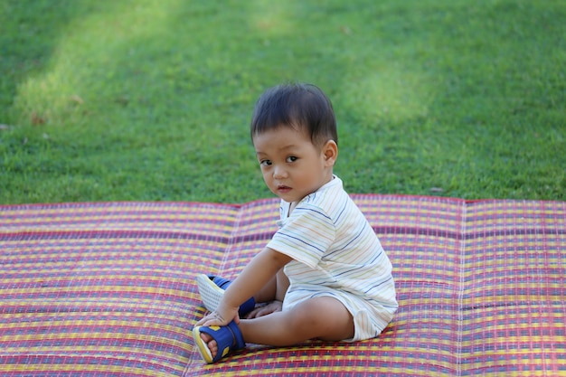 Il ragazzo asiatico sta sedendosi nel giardino.