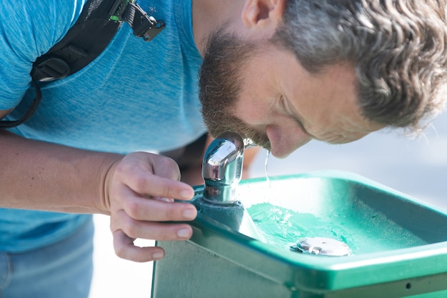 Il ragazzo assetato beve acqua dalla fontanella per dissetarsi, idratarsi.