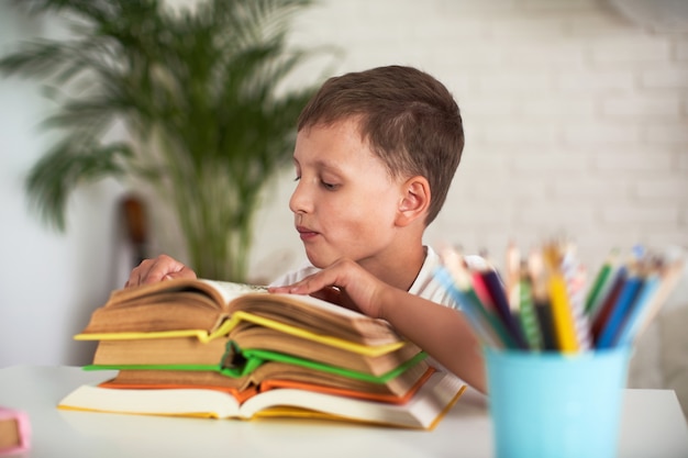 Il ragazzo attento è seduto al tavolo con una pila di libri