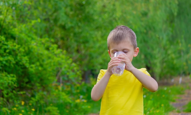 Il ragazzo beve l'acqua da un bicchiere Acqua pura Estate