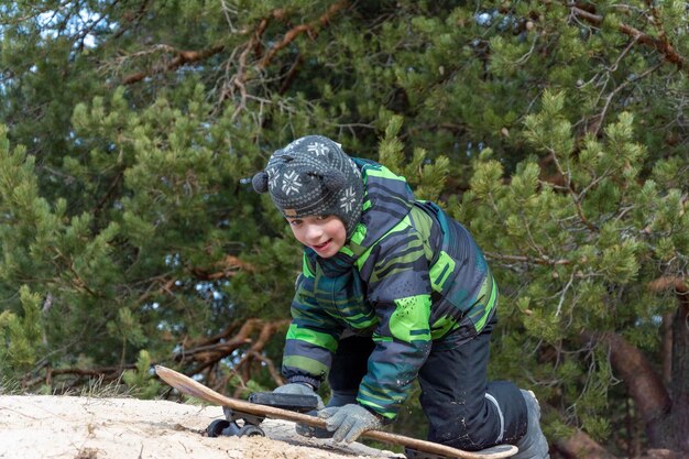 Il ragazzo bianco divertente si arrampica su una duna di sabbia con uno skateboard cammina nel parco