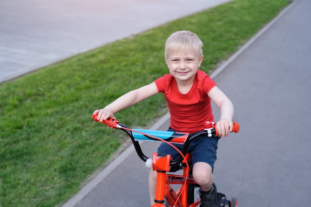Il ragazzo biondo bello guida su una bicicletta dei bambini