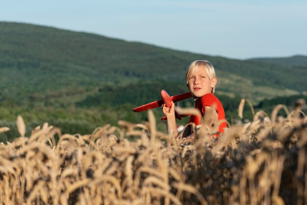 Il ragazzo biondo detiene il modello di un soggiorno in aereo sul campo di grano sullo sfondo della collina Campagna di fine settimana Il bambino sogna di viaggiare