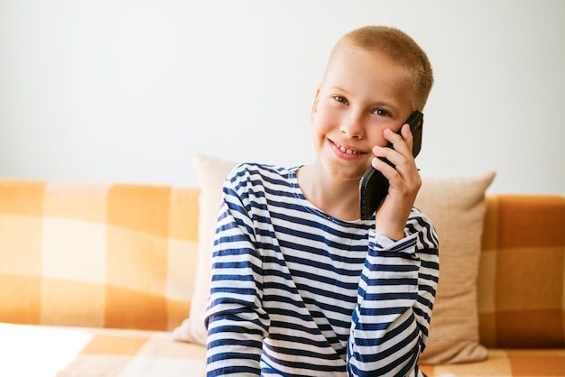 Il ragazzo biondo emotivo che parla al telefono si siede sul divano in abiti casual sorridendo chiacchierando con gli a...