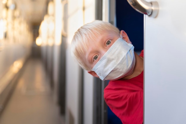 Il ragazzo biondo in maschera protettiva cavalca lo scompartimento del treno Viaggiando durante una quarantena Treno vuoto