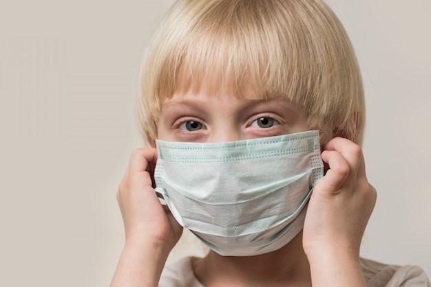 Il ragazzo biondo indossa una maschera medica sterile. Bambino che indossa una maschera protettiva contro l'influenza