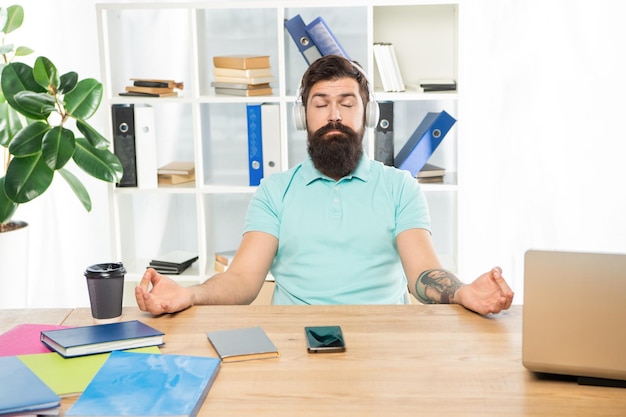 Il ragazzo calmo medita tenendo il mudra ascoltando musica rilassante in cuffia alla meditazione della scrivania dell'ufficio