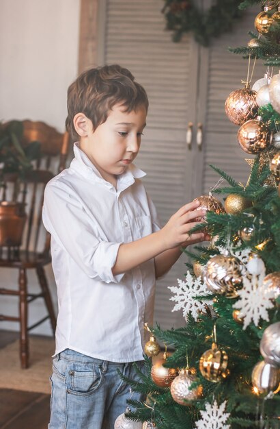 Il ragazzo carino di 8 anni in una camicia bianca adorna l&#39;albero di Natale