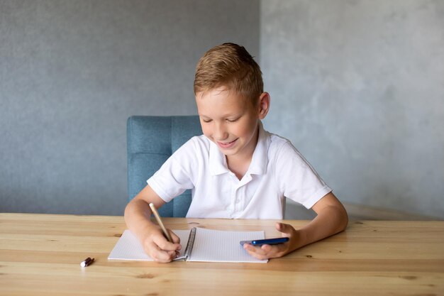 Il ragazzo carino scrive su un taccuino aperto e guarda il telefono