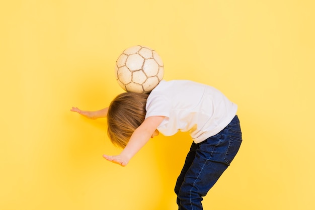 Il ragazzo carino tiene in mano una palla da calcio in vera pelle isolata su giallo