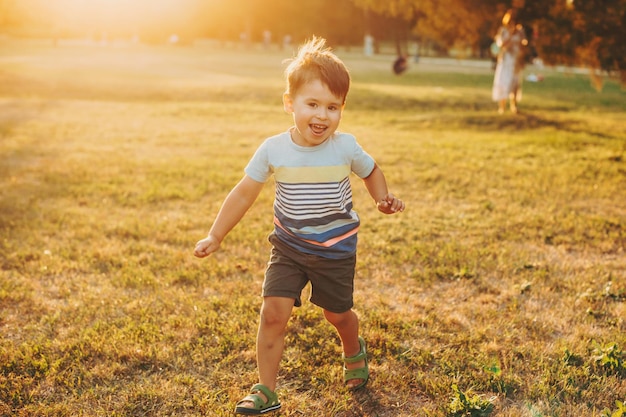 Il ragazzo caucasico corre lungo il campo sul tramonto della vista frontale dell'infanzia della telecamera