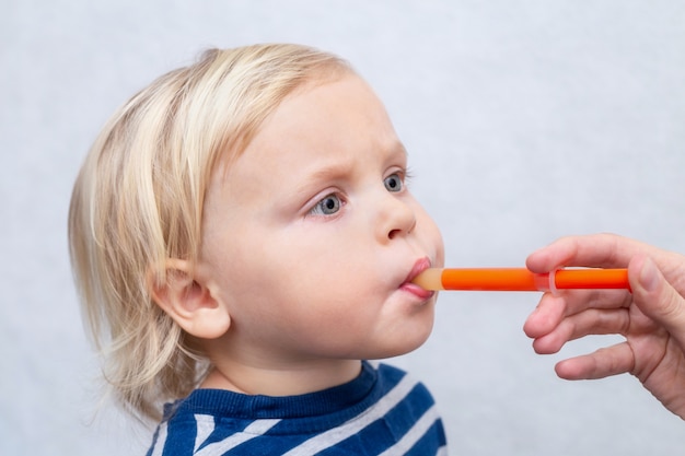 Il ragazzo caucasico sveglio ottiene la medicina dei bambini con una siringa nella sua bocca su bianco