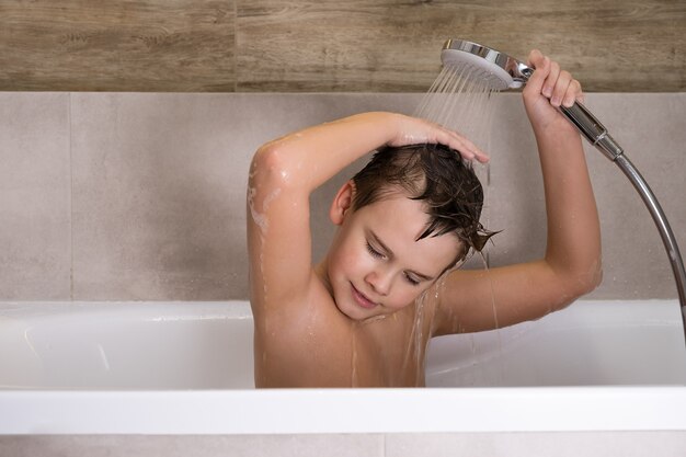 Il ragazzo che tiene il soffione della doccia e si lava la testa in bagno Felice infanzia sana