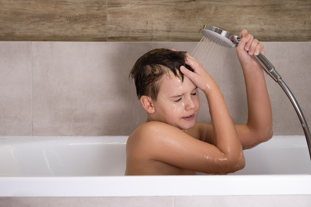 Il ragazzo che tiene il soffione della doccia e si lava la testa in bagno Felice infanzia sana