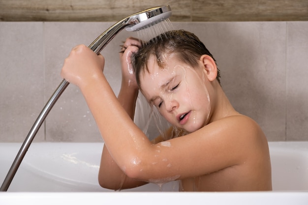 Il ragazzo che tiene la testa della doccia e si lava la testa in bagno infanzia sana healthy