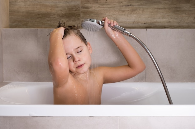 Il ragazzo che tiene la testa della doccia e si lava la testa in bagno infanzia sana healthy