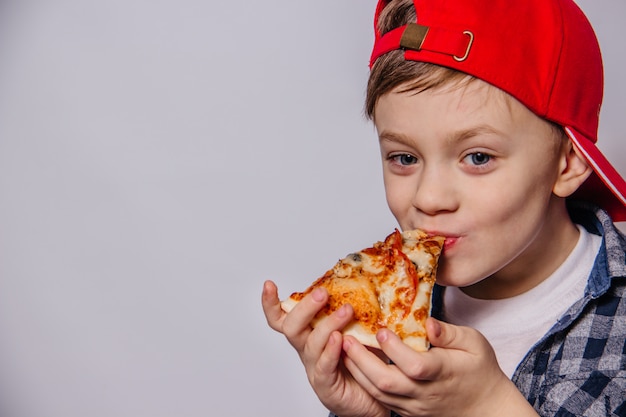 Il ragazzo con grande piacere mangia un pezzo di pizza