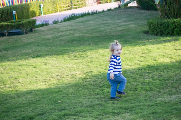 Il ragazzo con i capelli biondi corre sull'erba verde. Il bambino in abiti blu gioca in una giornata di sole. Concetto di infanzia felice. Attività, esperienza, apprendimento. Vacanze estive, avventura, scoperta.