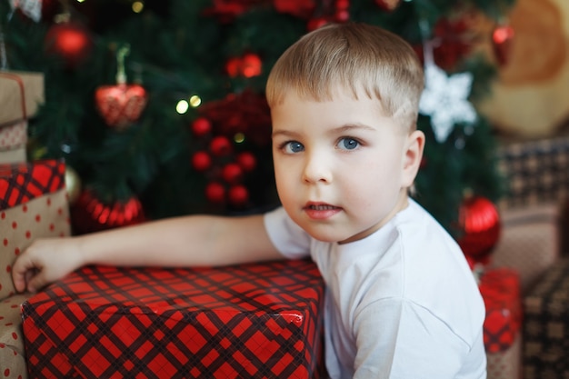 Il ragazzo con i cappelli di Natale è seduto con scatole regalo in mano con la gioia di una sorpresa.