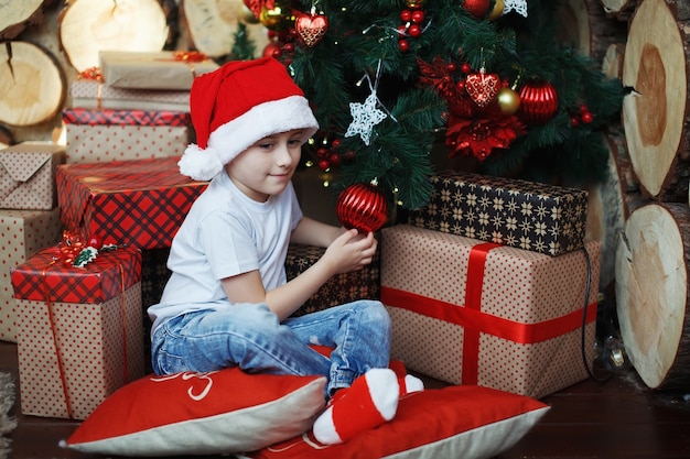 Il ragazzo con i cappelli di Natale è seduto con scatole regalo in mano con la gioia di una sorpresa.