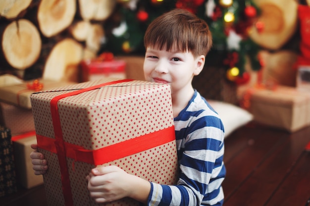 Il ragazzo con i cappelli di Natale è seduto con scatole regalo in mano con la gioia di una sorpresa.