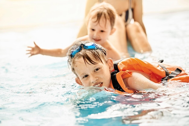 Il ragazzo con i googles e il giubbotto di sicurezza impara a nuotare vicino al fratello e alla mamma nella grande piscina del parco acquatico