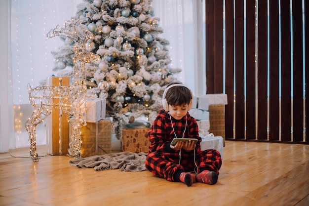 Il ragazzo con il telefono sotto lo stile di vita dell'albero di Natale. Capodanno e Natale.