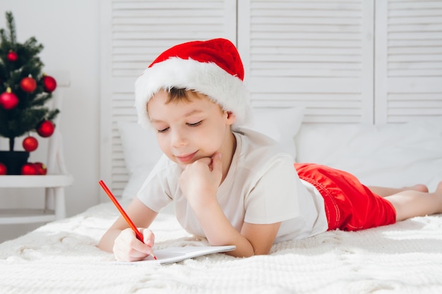 Il ragazzo con un berretto rosso scrive una lettera a Babbo Natale