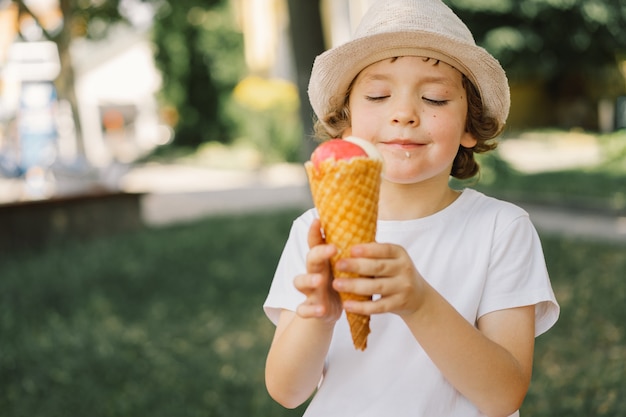 Il ragazzo con un cappello tiene in mano un gelato e sembra felice e sorpreso cibo estivo e ora legale