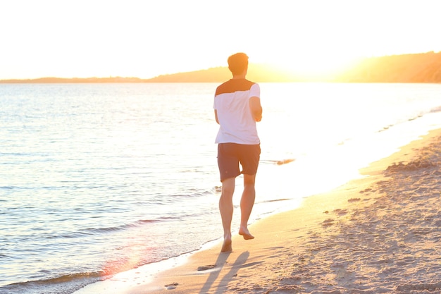 Il ragazzo corre lungo la riva del mare contro il tramonto