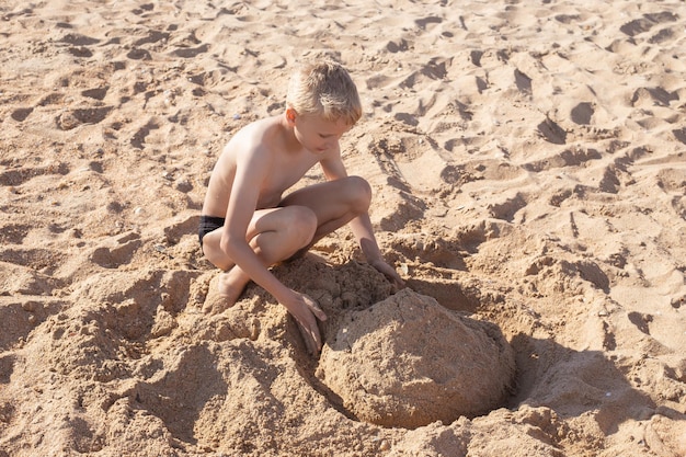 Il ragazzo costruisce un castello di sabbia in riva al mare Vacanze estive giochi e divertimento in mare