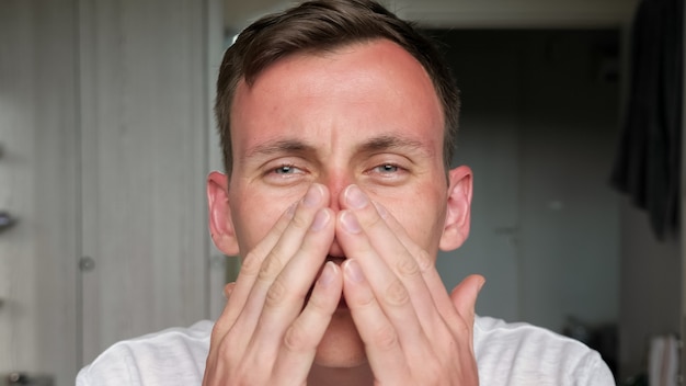 Il ragazzo dagli occhi blu con un taglio di capelli corto sembra dritto e tocca il viso bruciato dal sole seduto a casa contro i muri e il primo piano della porta