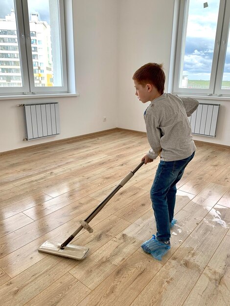 Il ragazzo dai capelli rossi del bambino lava il pavimento in un nuovo stile di vita dell'appartamento il concetto di trasferirsi in una nuova pulizia della casa