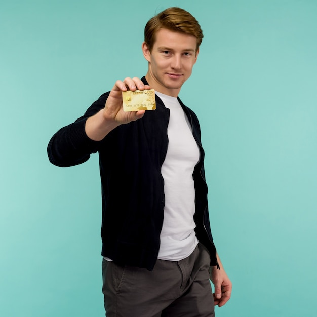 Il ragazzo dai capelli rossi sportivo bello tiene una carta di credito dell'oro
