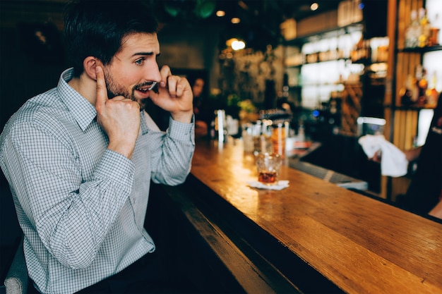 Il ragazzo dai capelli scuri è seduto allo stand del barista e parla al telefono