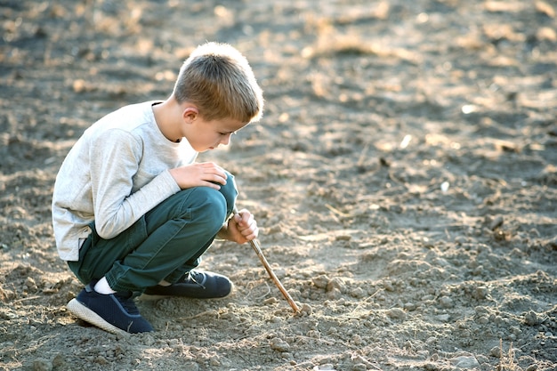 Il ragazzo del bambino che gioca con il bastone di legno che scava nella sporcizia nera ha frantumato all'aperto.