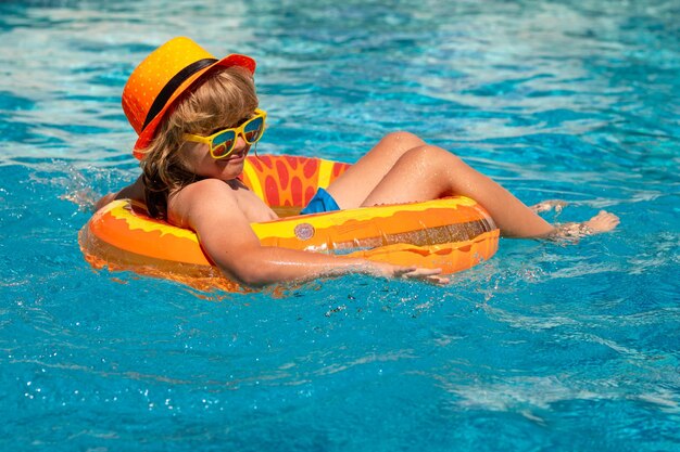 Il ragazzo del bambino che nuota nella piscina gioca con l'anello galleggiante sorridente il bambino sveglio in occhiali da sole nuota con il gonfiabile