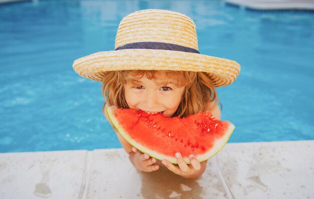 Il ragazzo del bambino mangia l'anguria vicino al bambino della piscina con le attività estive dei bambini dell'anguria