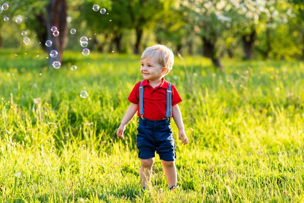 Il ragazzo del bambino si diverte a giocare in natura con bolle di sapone lucide