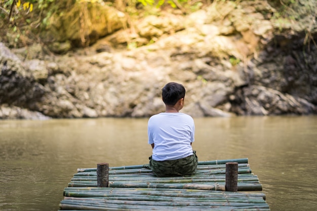 Il ragazzo del bambino si siede sul ponte di bambù accanto al lago