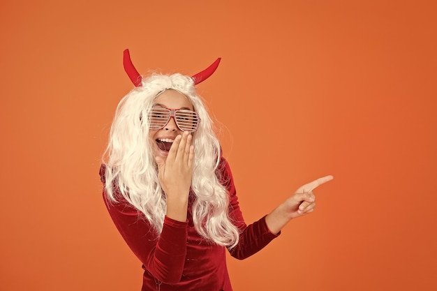 Il ragazzo del diavolo di Halloween con le corna da diavoletto indossa gli occhiali da festa e punta il dito sullo spazio della copia felice halloween