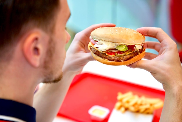 Il ragazzo del giovane è seduto sulla food court tenendo in mano mangiare succosi hamburger hamburger fast food