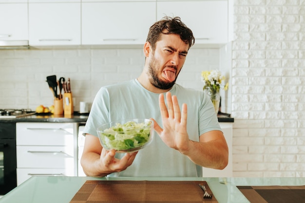 Il ragazzo del giovane è stufo del cibo sano sotto forma di verdure e smorfie di verdure alla vista di a