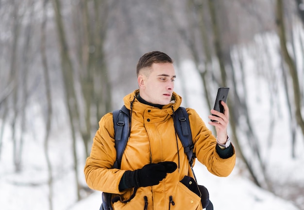 Il ragazzo del turista controlla se c'è una connessione al telefono mentre cammina nella fredda foresta invernale