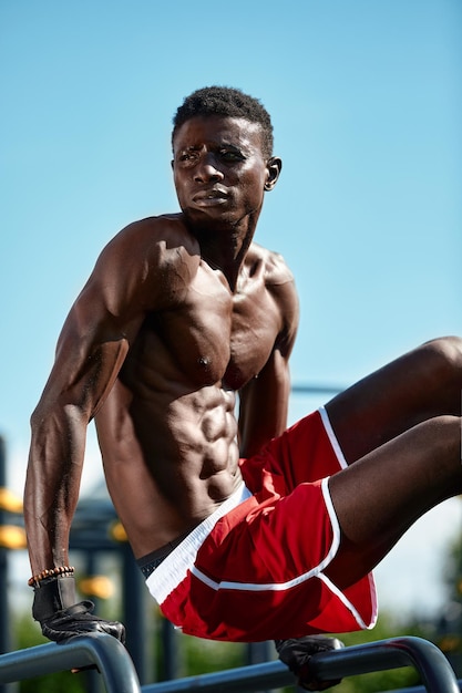 Il ragazzo dell'atleta afroamericano fa esercizi di fitness calisthenics sulle barre nel parco