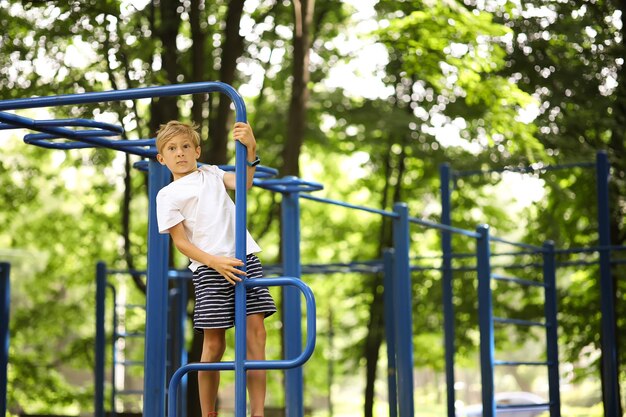 Il ragazzo dell'atleta nel parco fa sport appeso alle mani e fa esercizi sulle barre irregolari con le gambe incrociate