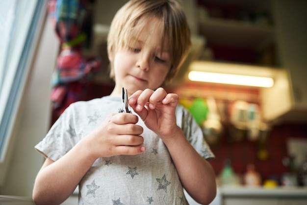 Il ragazzo di 6 anni crea artigianato a casa. Tiene in mano una pinza e un bastone di legno